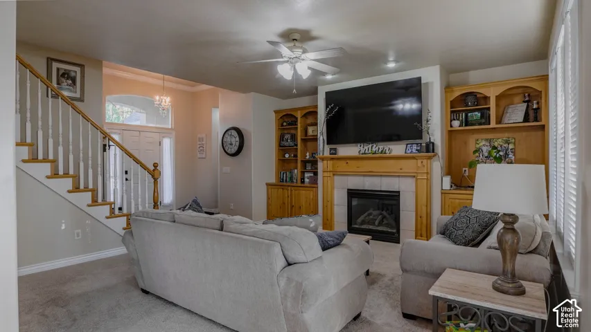 Living area featuring a fireplace with a wood mantel and tile surround, custom built-in cabinetry, an open staircase with a wooden handrail and white balusters, and a ceiling fan