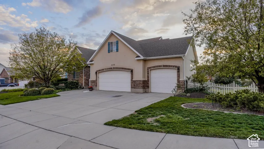 Stucco exterior featuring stone accents, gabled rooflines, two-car garage, and white picket fencing