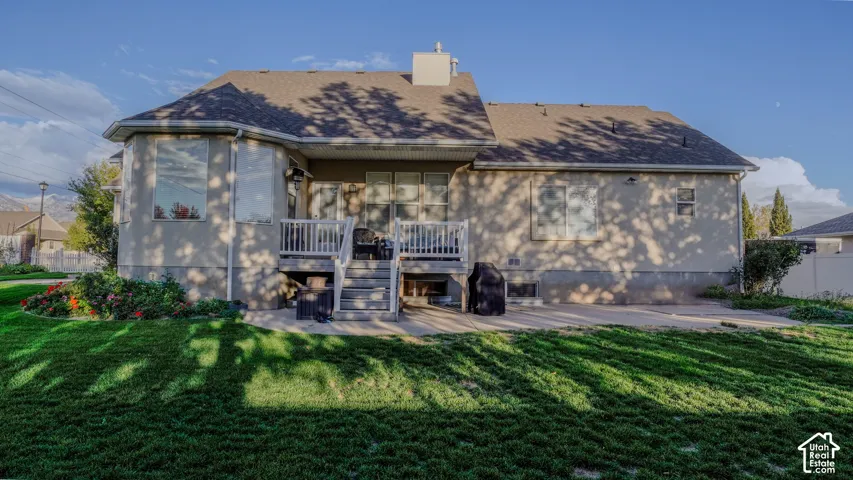 Rear exterior featuring a raised wood deck with white railings, a concrete patio, stucco siding, and a multi-pitched asphalt shingle roof