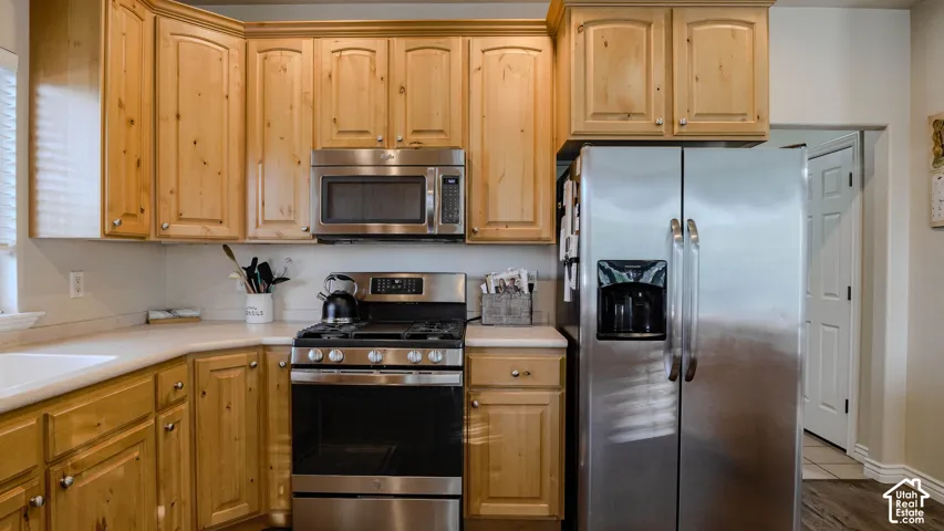 Kitchen featuring natural wood cabinetry, solid-surface countertops, and stainless steel appliances including a gas range, over-the-range microwave, and side-by-side refrigerator