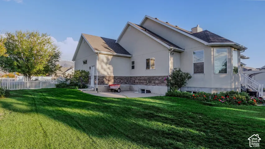Multi-level exterior featuring stucco siding, stone veneer accents, architectural roof shingles, a paved patio, and white vinyl perimeter fencing
