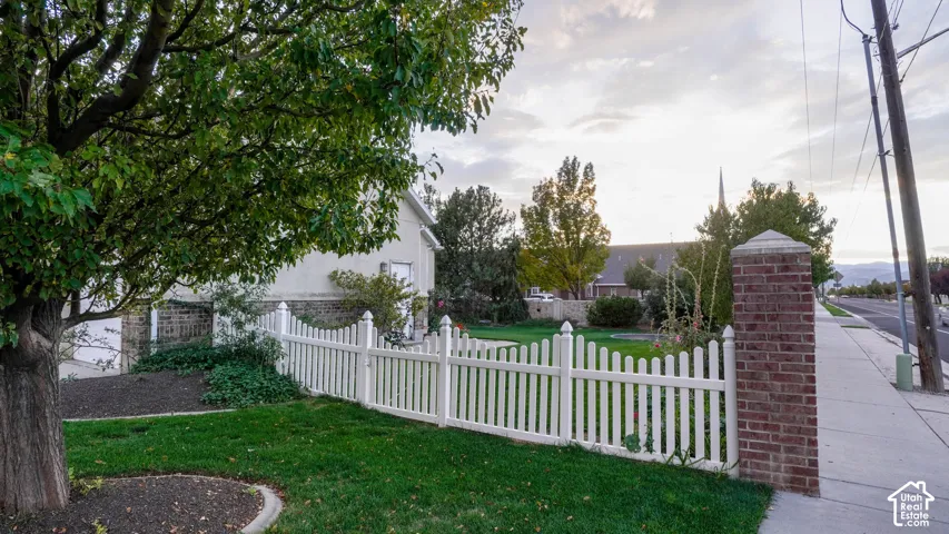 Manicured lawn area enclosed by a white picket fence, anchored by a brick masonry pillar and mature landscaping