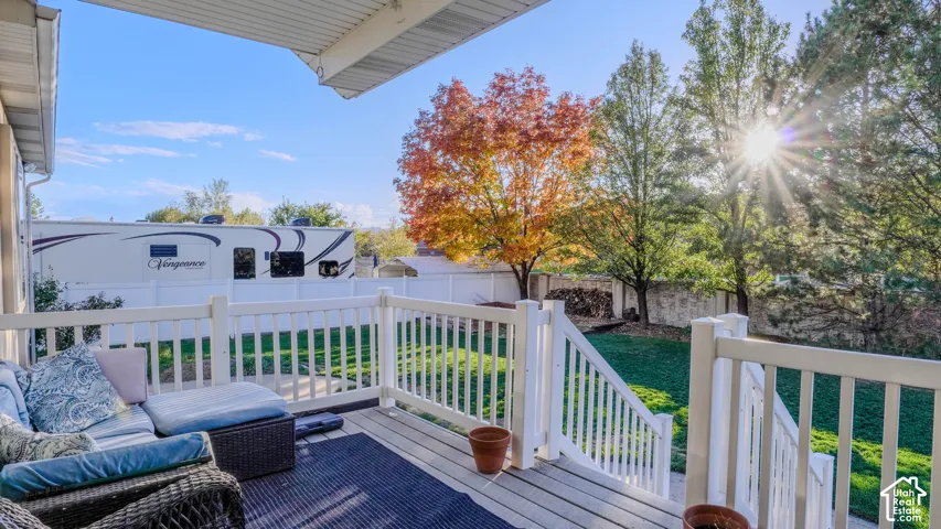 Covered deck featuring a white railing, staircase, and wood-finish decking overlooking a fenced backyard with mature trees
