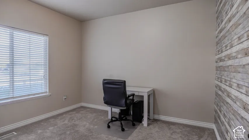 Neutral-toned interior space featuring a textured wood-panel accent wall, carpeted flooring, and a window with horizontal blinds
