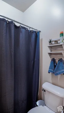 Bathroom featuring a standard toilet and a shower area with a curtain rod and integrated wall shelving