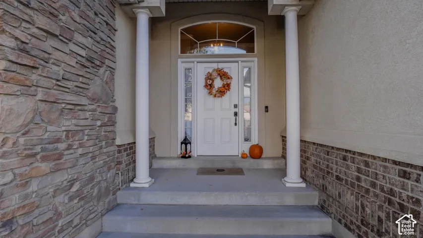 Covered entryway featuring stone veneer siding, brick accent trim, two structural columns, and a multi-panel front door with sidelights and an arched transom window
