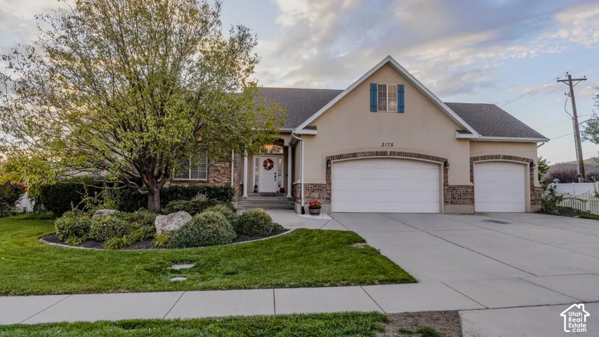 Exterior facade featuring a stucco finish, stone veneer accents, three-car garage, and a gable roofline