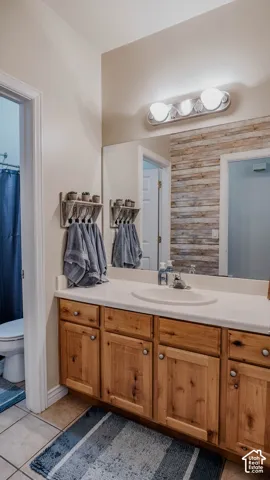 Wood cabinetry vanity with an integrated countertop and sink, large wall-mounted mirror, decorative wood-plank accent wall, and three-bulb vanity lighting