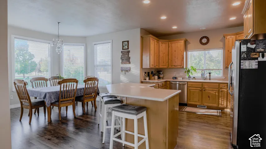 Kitchen featuring wood cabinetry, solid-surface countertops, wood-finish flooring, recessed lighting, and a center island with a breakfast bar