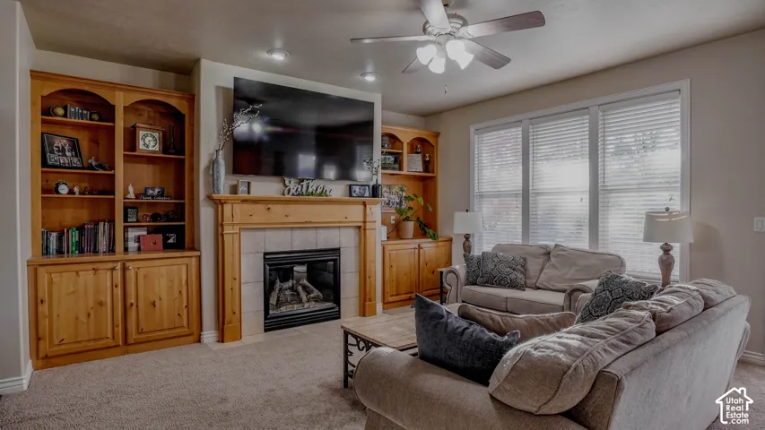 Fireplace with tile surround and wood mantel, flanked by custom wood built-in cabinetry, recessed lighting, and a ceiling fan