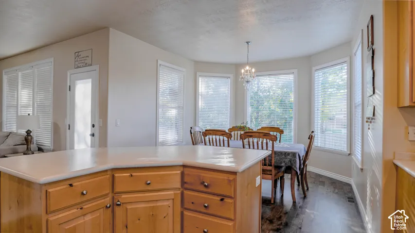 Kitchen featuring wood cabinetry, a solid-surface island countertop, bay windows, wood-finish flooring, and a suspended chandelier