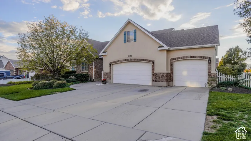 Stucco and brick facade with a three-car garage, concrete driveway, and manicured landscaping