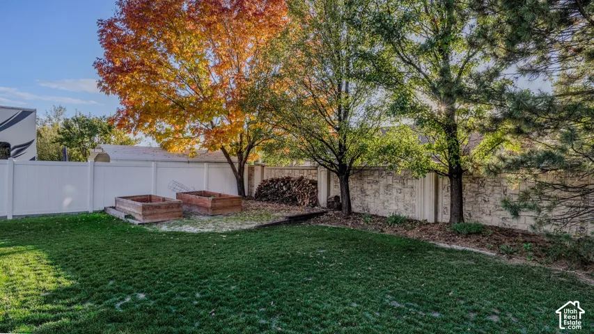 Backyard featuring a manicured lawn, stone perimeter wall, white privacy fencing, and two raised garden beds