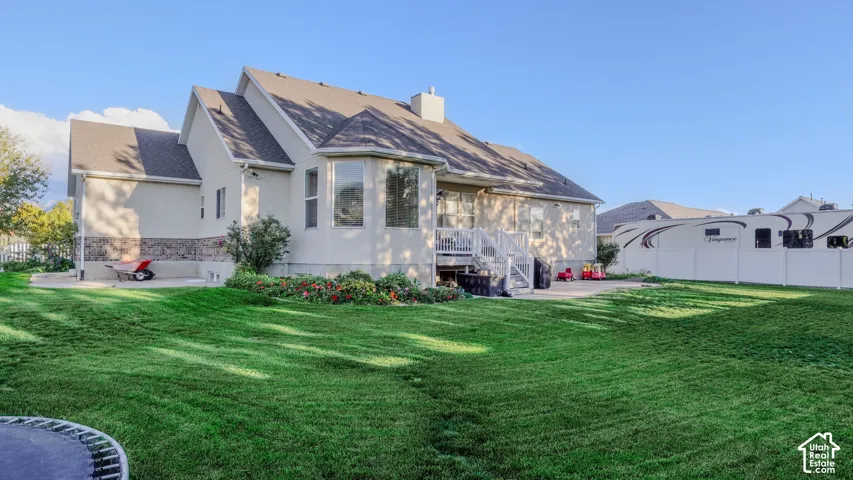 Rear exterior featuring a multi-gabled roofline, stone veneer foundation accents, raised wood deck with white railings, concrete patio, and a privacy fence