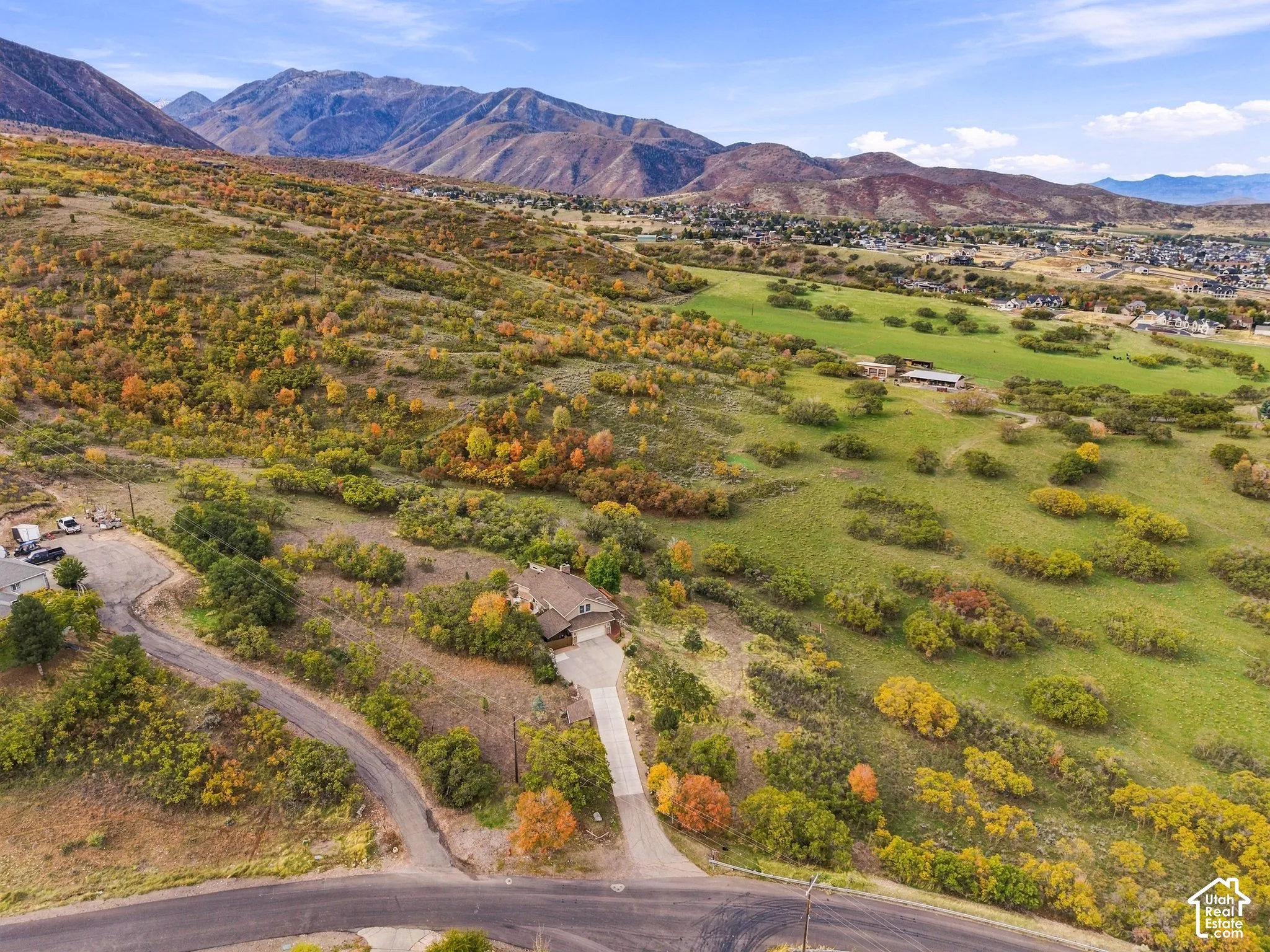 Aerial perspective featuring expansive acreage, a multi-pitched roofline, a paved concrete driveway, and a mountainous backdrop