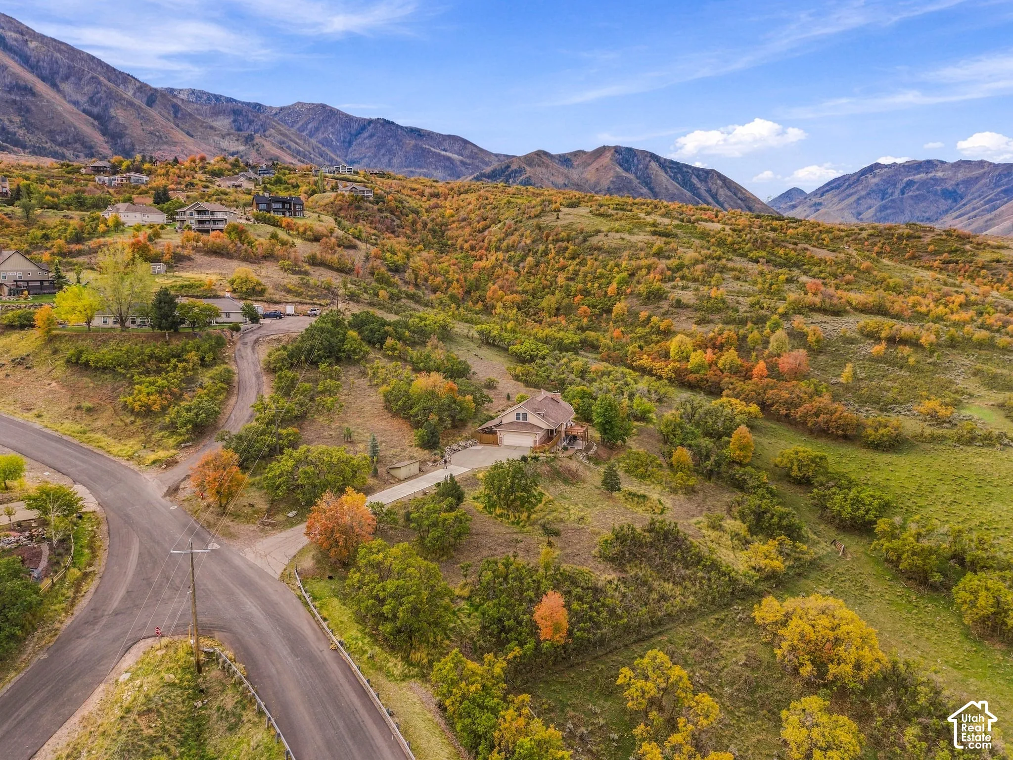 Aerial perspective of a multi-level residence featuring a multi-car garage, concrete driveway, and expansive natural terrain backdropped by mountain ranges