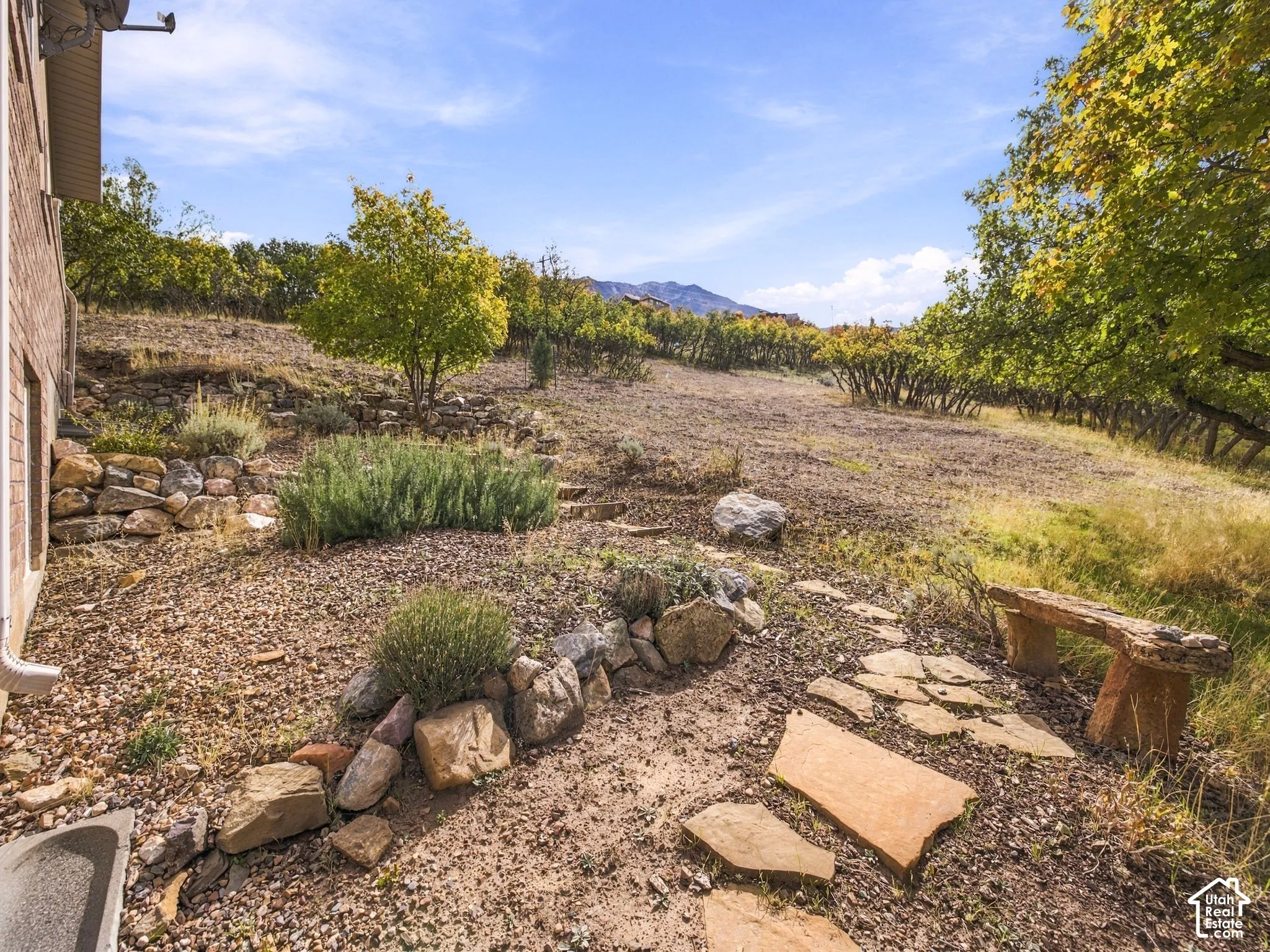 Terraced natural stone retaining walls, flagstone path, and mature tree landscaping set against a mountain backdrop