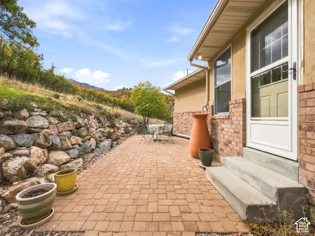 Paver patio featuring a natural stone retaining wall, brick and stucco exterior finish, concrete steps, and mountainous backdrop