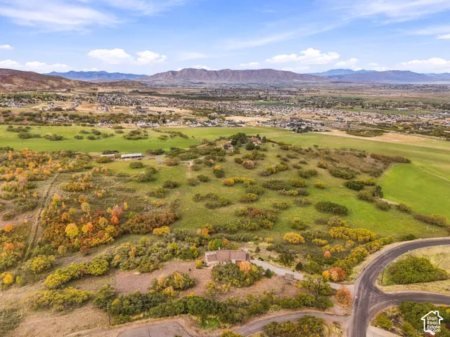 Aerial perspective of a sprawling property featuring mountainous terrain, rolling topography, mature trees, and paved road access