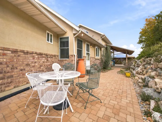 Exterior featuring a brick and stucco facade, expansive paver patio, covered carport, and rock-lined landscaping