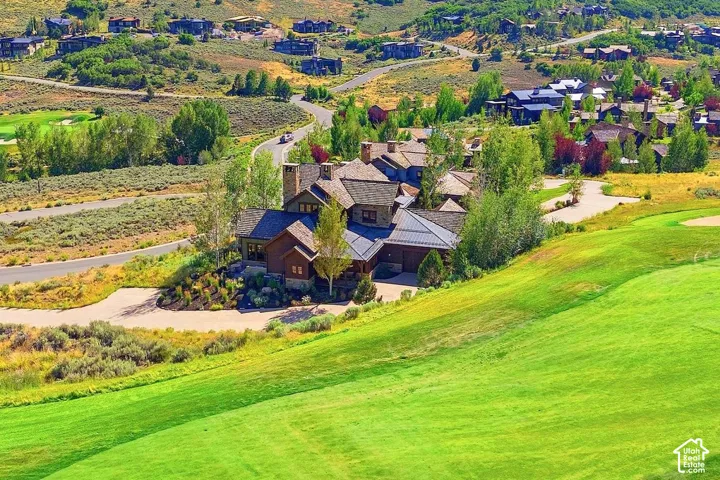 Multi-level mountain residence featuring stone and wood-shake exterior cladding, steep-pitched gable rooflines, multiple masonry chimneys, and a private driveway, situated on a sprawling hillside golf course lot