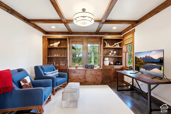 Custom stained wood ceiling beams, integrated wood cabinetry, built-in shelving, dark wood-finish flooring, and a multi-tiered drum chandelier