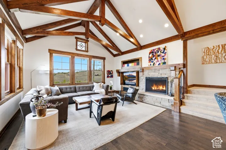 Vaulted ceiling with exposed wood beams, stone-surround fireplace, built-in media cabinetry, wood-finish flooring, and multi-pane windows