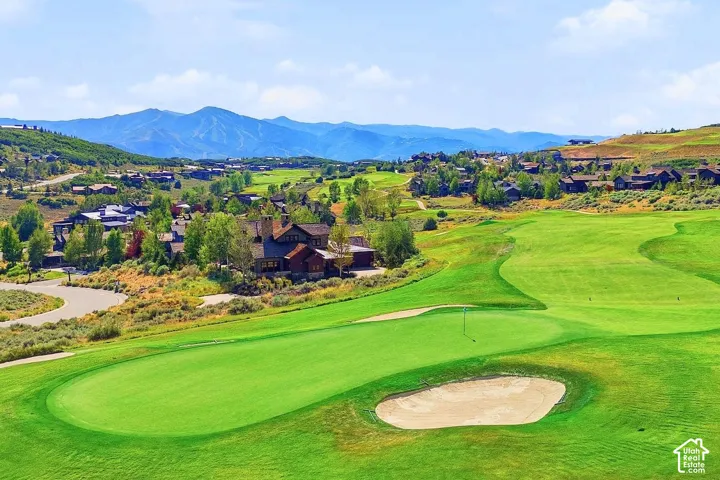 Multi-story residence featuring stone and timber exterior siding, situated on a golf course with mountainous backdrop