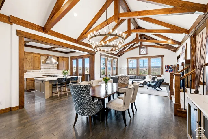 Vaulted ceiling with exposed wood trusses, wood-finish flooring, central iron chandelier, and custom cabinetry
