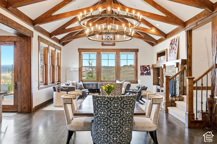 Vaulted ceiling with exposed wood trusses, large-scale circular iron chandelier, wood-trimmed windows, hardwood flooring, and floor-to-ceiling stone fireplace surround