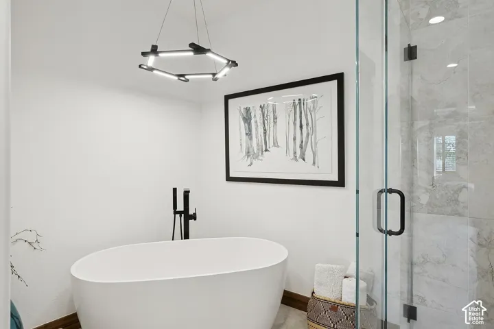 Freestanding soaking tub featuring a matte black floor-mounted faucet, geometric LED pendant lighting, and a walk-in shower with stone-finish tile surround and matte black hardware