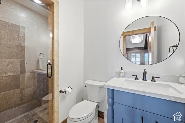 Bathroom featuring a blue vanity with a stone countertop, an integrated rectangular sink, oil-rubbed bronze fixtures, a walk-in shower with stone tile surround, and an oval wall-mounted mirror