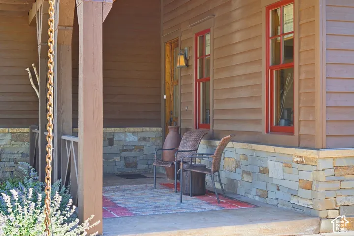 Covered entryway featuring horizontal wood-finish lap siding, multi-tonal stacked stone wainscoting, double-hung windows with red trim, and a decorative metal rain chain