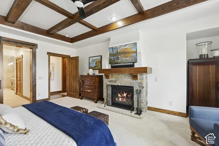 Coffered ceiling with exposed wood beams, stone-faced fireplace with a natural wood mantel, and wood-trimmed door casings