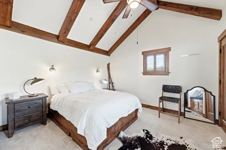 Vaulted ceiling featuring exposed timber beams, integrated ceiling fan, wall-mounted sconce lighting, and wood-trimmed window casing