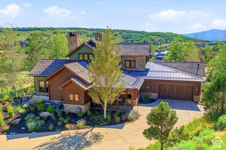 Multi-level exterior featuring wood siding, natural stone accents, a dark metal roof, dual stone chimneys, and a multi-car garage