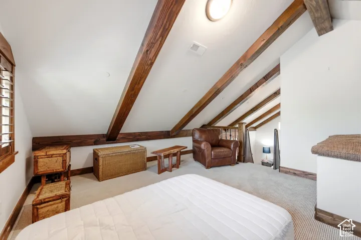 Vaulted ceiling featuring exposed wood beams, wall-to-wall carpeting, and wood-trimmed window casing