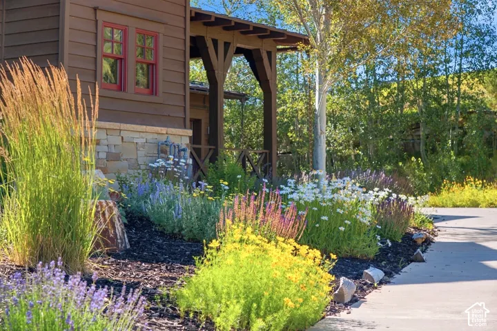 Exterior facade featuring horizontal wood siding, natural stone accents, covered porch with timber framing, red-framed windows, and professional perennial landscaping