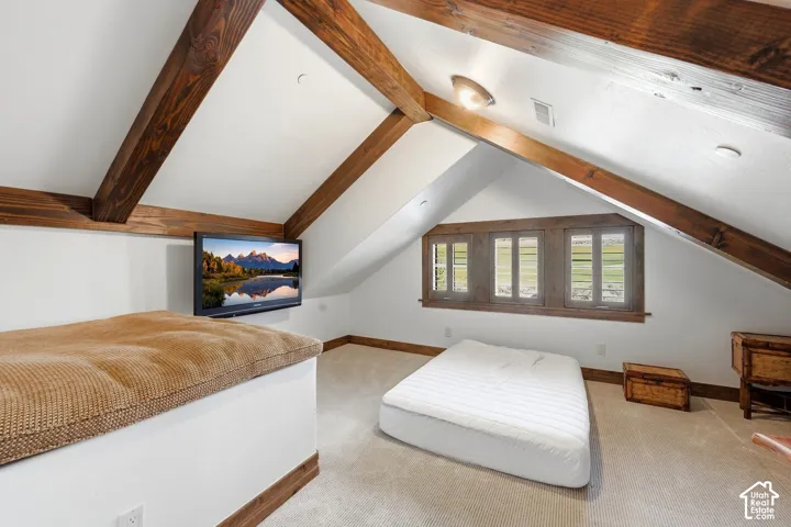 Vaulted ceiling with exposed wood beams, triple window configuration with wood trim, and wall-to-wall carpeting