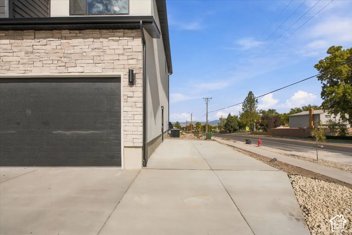 Exterior facade featuring stacked stone veneer, vertical siding, concrete driveway, and a multi-panel garage door with wall-mounted exterior lighting