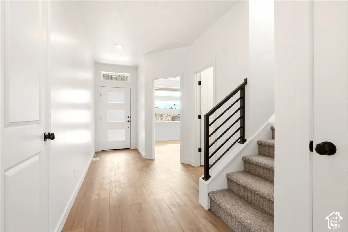 Entryway featuring light-toned wood-finish flooring, a white front door with three rectangular frosted glass panels, and a staircase with a matte black metal railing and neutral carpeting