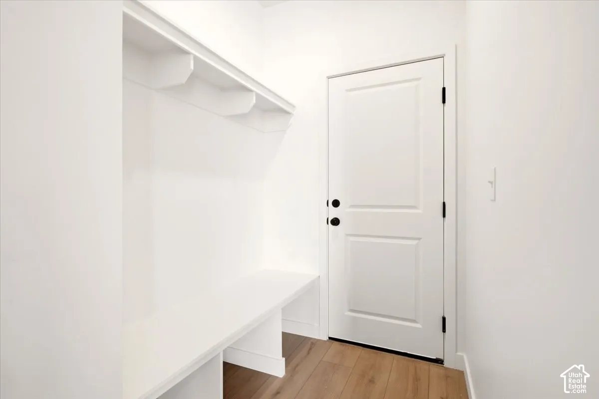 Built-in storage bench and overhead shelving, wood-finish flooring, paneled door, and matte black hardware