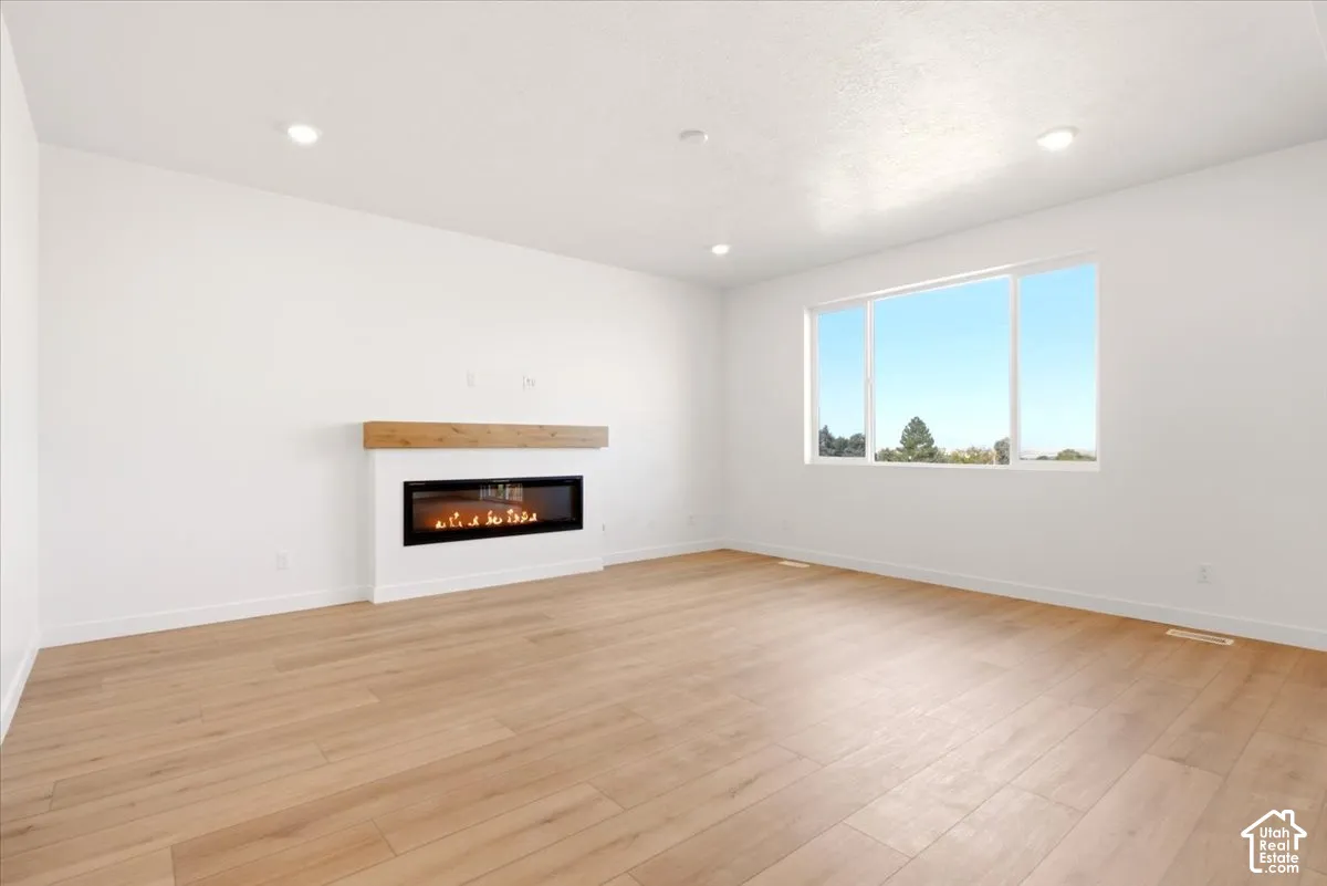 Living area featuring wood-finish flooring, recessed lighting, and a linear electric fireplace with a wood mantel