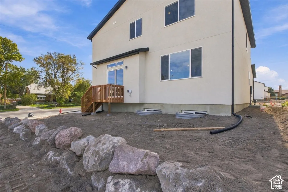 Stucco exterior featuring a wood deck, large slider, two egress window wells, and a natural stone retaining wall