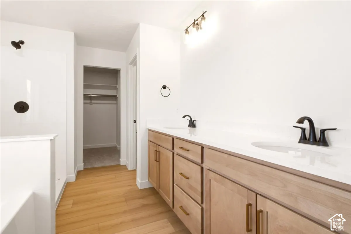 Dual-sink vanity with light wood-finish cabinetry, stone-composite countertop, matte black fixtures, and wood-finish flooring