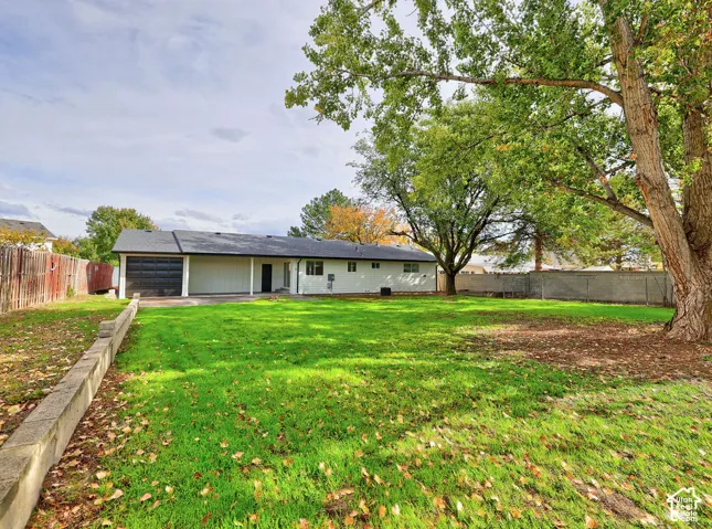 Expansive backyard featuring a sprawling lawn, mature trees, a concrete retaining wall, and full perimeter fencing