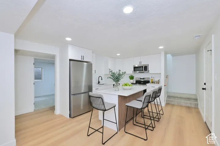 Kitchen featuring white cabinetry, quartz countertops, a central island with wood-slat detailing, stainless steel appliances, and wood-finish flooring