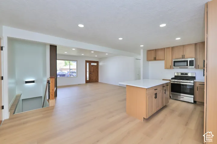 Open-concept interior featuring wood-finish flooring, recessed lighting, a center kitchen island with a quartz countertop, light wood cabinetry, and stainless steel appliances
