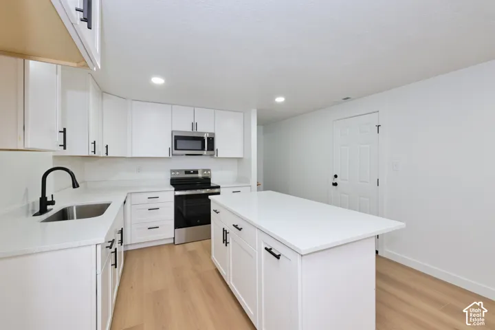 Kitchen featuring white shaker-style cabinetry, quartz countertops, stainless steel appliances, a central island, and wood-finish flooring