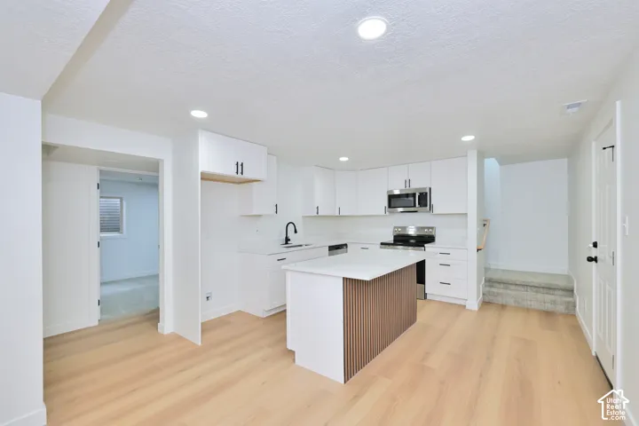 Kitchen featuring white shaker-style cabinetry, wood-finish flooring, a center island with fluted detailing, stainless steel appliances, and recessed lighting
